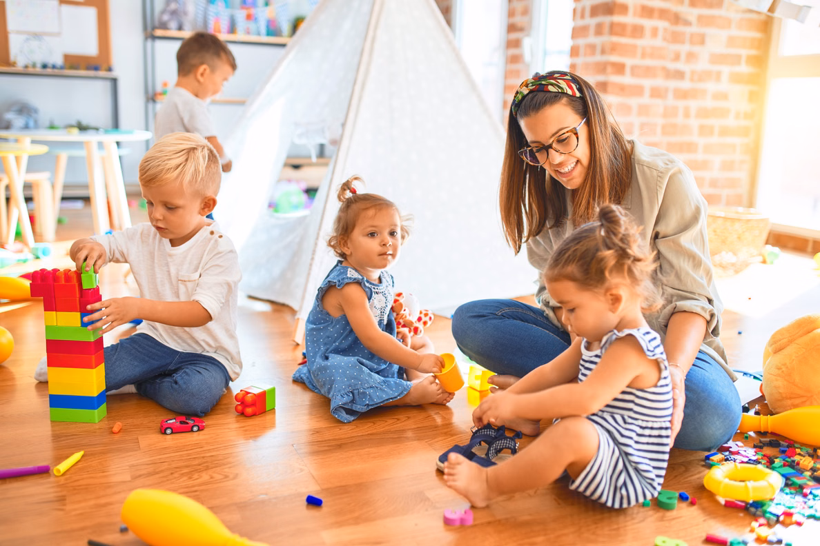 Eine Frau speilt mit vier Kindern mit bunten Bauklötzen