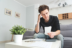 Junger Mann der nachdenklich, grübelnd schaut, während er seine Finanzen anschaut.
