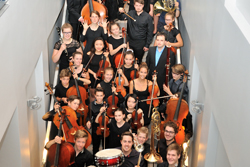 Viele Menschen stehen mit Instrumenten in einem Gang, es wird von oben fotografiert.