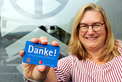 eine blonde lächelnde Frau hält eine Ehrenamts-Card in die Kamera
