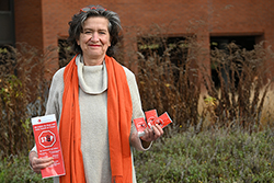 eine Frau mit orangem Schal hält einen Flyer und Taschentücher mit der Aufschrift 
