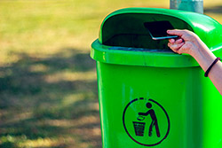 Eine Hand, die ein Smartphone in einer Mülleimer legt