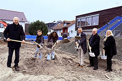 Ein Gruppenfoto bei der Frauen, Kinder und Männer mit einer Schaufel etwas Sand schaufeln