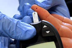 Finger mit Blutstropfen bei einer Blutzuckermessung mit Messgerät