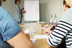 Drei Frauen sitzen am Schreibtisch und hören sich einen Vortrag an
