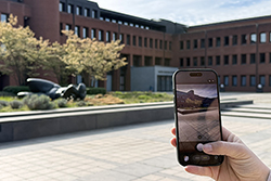 Eine Hand hält ein Smartphone in der Hand und richtet es vor ein Kunstwerk im Landratsamt