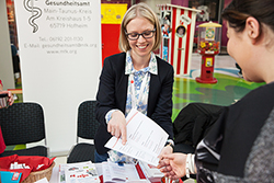 eine Frau, die an einem Stand Broschüren verteilt.