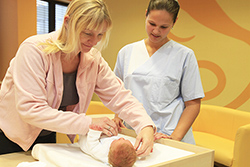eine Frau, die einer anderen zeigt, wie man ein Baby wickelt.