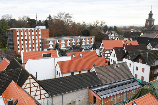 den Blick über die Dächer eines Ortes mit einem großen, rot-weißen Gebäude im Hintergrund