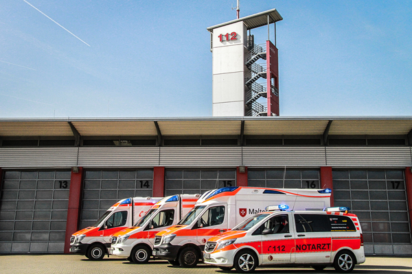 Mehrere Rettungs- und Notarztwagen vor einem Gebäude, hinter dem ein Turm mit der Aufschrift 112 steht.