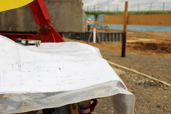 im Vordergrund einen ausgebreiteten Bauplan und im Hintergrund eine Baustelle.
