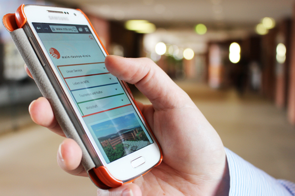 eine Hand, die ein Smartphone hält, auf dem die Internetseite des Main-Taunus-Kreises angezeigt wird.