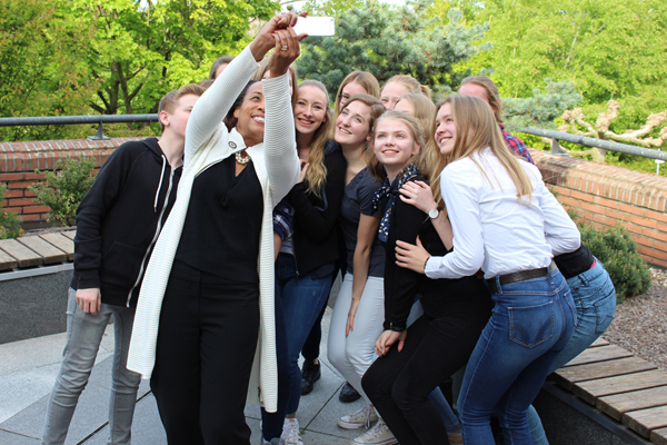 eine Frau mit einer Gruppe Jugendlicher, die sich selbst mit dem Handy fotografieren.