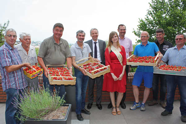 neun Männer, von denen viele Schalen mit Erdbeeren in der Hand halten, und in der Mitte eine Frau im roten Kleid.