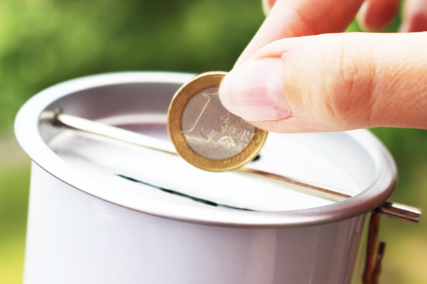 eine Hand, die eine Euro-Münze in eine Sammelbüchse wirft.