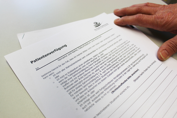 Papiere mit dem Titel Patientenverfügung auf einem Tisch, die von einer Hand festgehatlen werden