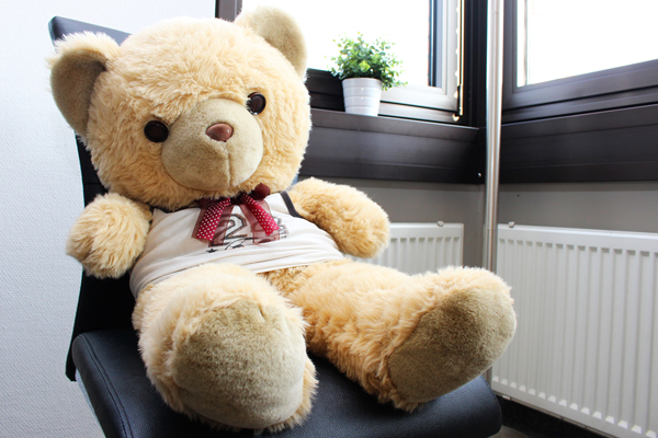 einen hellbraunen Teddybär mit weißem T-Shirt, der auf einem Stuhl sitzt