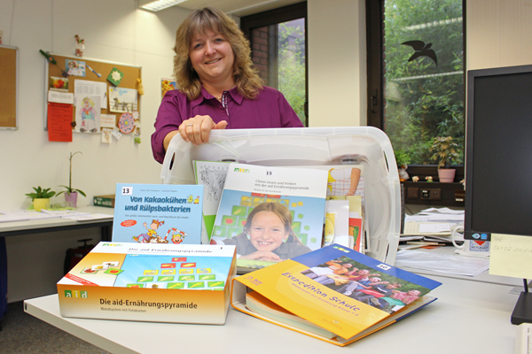 eine Frau, die eine Kiste voller Ordner, Bücher und anderer Unterlagen präsentiert