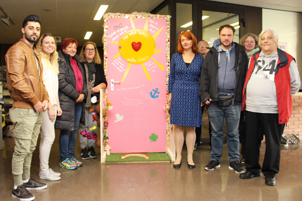 eine Gruppe Personen steht um eine rosa gestrichene und künstlerisch verzierte Tür