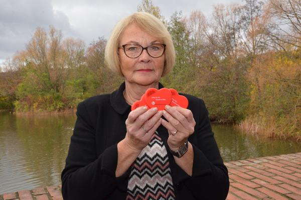 eine Frau vor einem Teich, die rot eingepackte Pfefferminz-Herzen in die Kamera hält