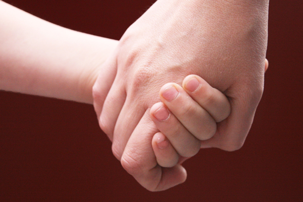die Großaufnahme einer Kinder- und einer größeren Hand, die einander festhalten