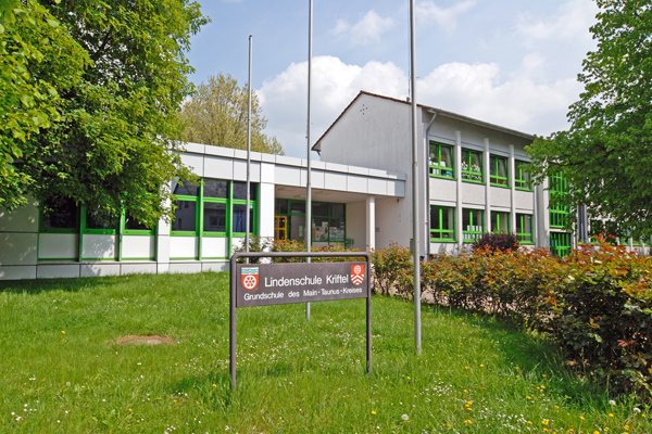 Blick über eine Wiese auf ein Schulgebäude und einem Schild mit der Aufschrift Lindenschule Kriftel im Vordergrund