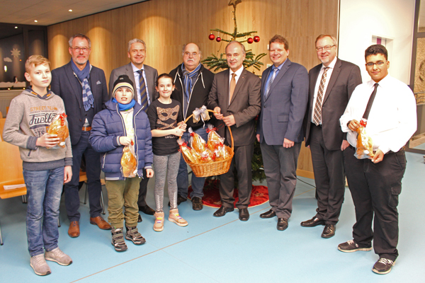 Zehn Personen stehen in einer Reihe vor einem geschmückten Weihnachtsbaum und schauen zur Kamera. Die Person in der Mitte hält einen Korb mit Gebäck in der Hand.