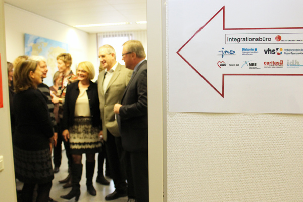 mehrere Personen im Gespräch in einem Raum, neben dessen Tür ein Schild mit der Aufschrift Integrationsbüro hängt.