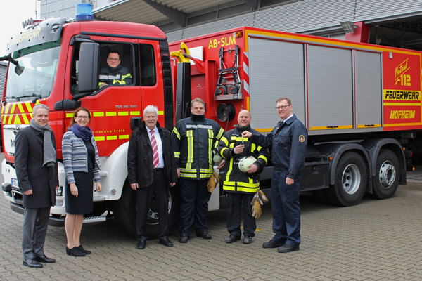 ein Feuerwehr-Transportfahrzeug, in dem ein Mann sitzt und vor dem fünf Männer und eine Frau stehen und in die Kamera schauen