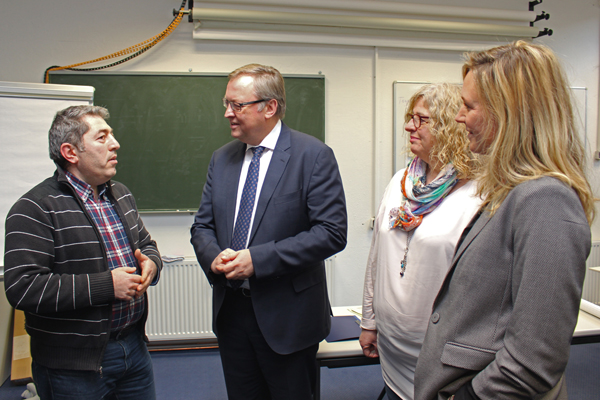 zwei Frauen und zwei Männer im Gespräch in einem Klassenraum mit Tafel im Hintergrund