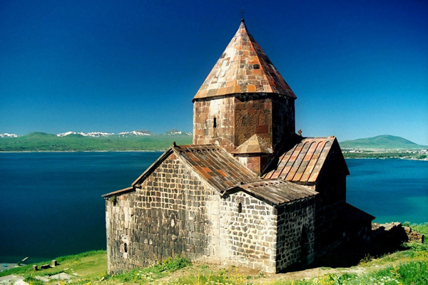 eine kleine Kirche aus Stein, die vor einem See im Grünen liegt