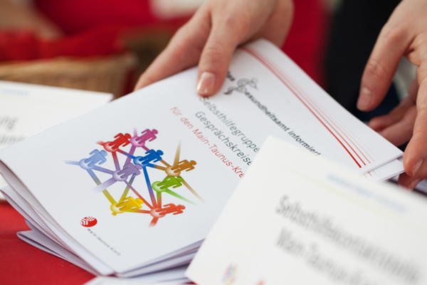 Hände, die einen Stapel Broschüren mit Informationen zu Selbsthilfegruppen von einem Tisch hochheben