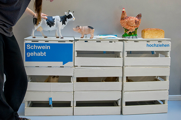 Figuren mehrere Tiere auf einem Regal, davor angeschnitten eine Person, die eine Hand auf die Figur einer Kuh gelegt hat