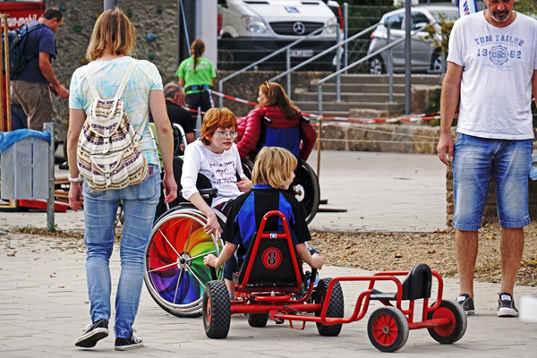 Kinder, Jugendliche und Erwachsene in Rollstühlen und auf Kettcars in einem Hof