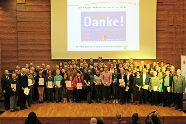 eine große Gruppe Menschen auf einer Bühne, viele von ihnen mit Urkunden in der Hand; im Hintergrund ist groß das Wort Danke eingeblendet