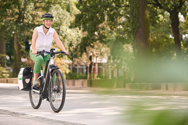 eine Frau in Freizeitkleidung und mit Fahrradhelm auf einem Fahrrad in einer schmalen Straße