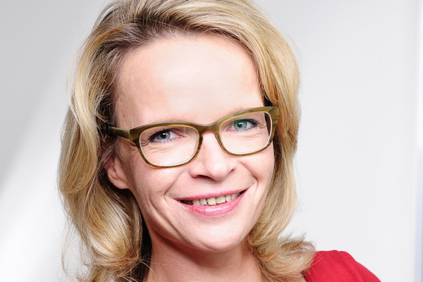 Portrait einer Frau mit blonden Haaren, Brille und rotem Oberteil