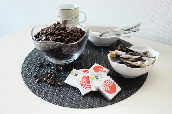 mehrere Schalen mit Kaffeebohnen, Zucker und Löffeln, einige kleine Tafeln Schokolade und ein Kaffeebecher auf einem Tisch