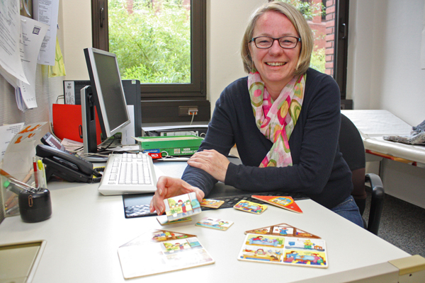 eine blonde Frau mit Brille an einem Schreibtisch, die buntes Kinderspielzeug in der Hand hält