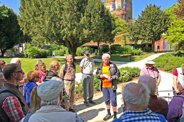 eine Gruppe Wanderer, die im Halbkreis in einem Park vor einem Gebäude stehen
