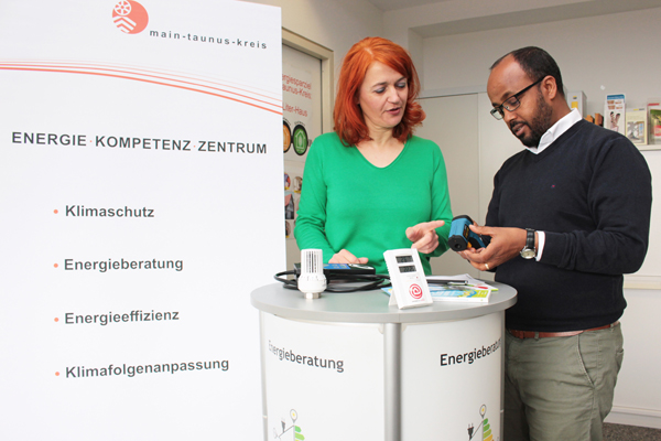 ein Mann und eine Frau im Gespräch an einem Stehtisch, daneben ein Plakat mit Werbung für eine Energieberatung