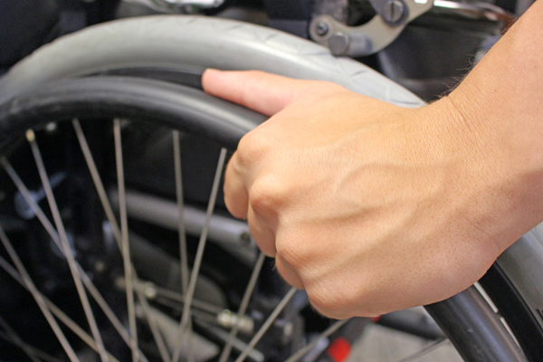 die Hand eines Rollstuhlfahrers, die an das Rad des Rollstuhls greift