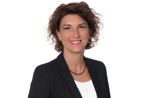 Portrait einer Frau mit kurzen, braunen, lockigen Haaren, die in die Kamera lächelt