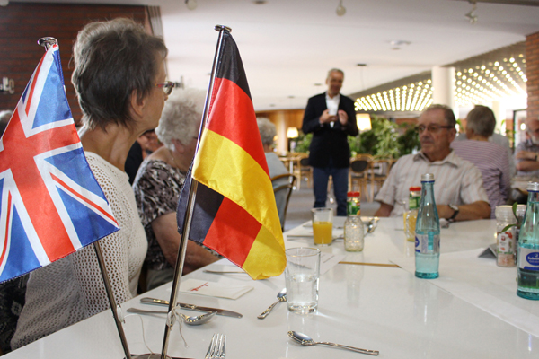 eine britische und eine deutsche Flagge auf einem Tisch, an dem mehrere Personen sitzen