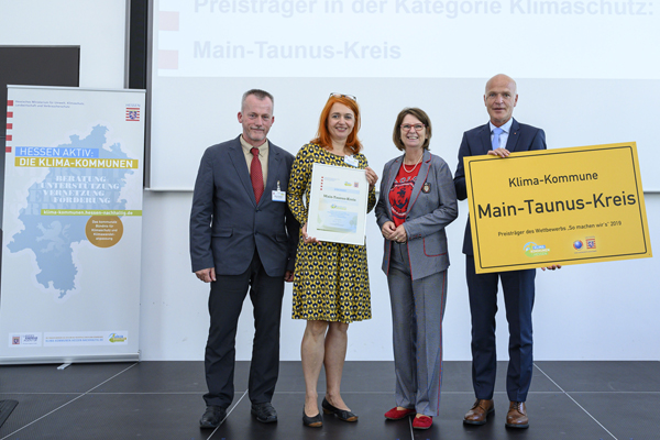 zwei Männer und zwei Frauen mt einer Urkunde und einem großen Schild mit der Aufschrift Klima-Kommune Main-Taunus-Kreis