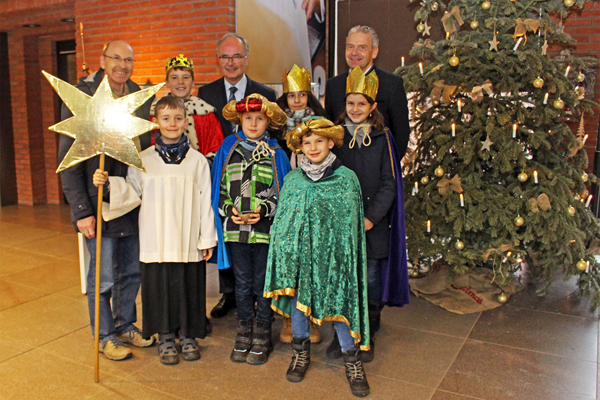 sechs als Sternsinger verkleidete Kinder und drei Männer neben einem Weihnachtsbaum