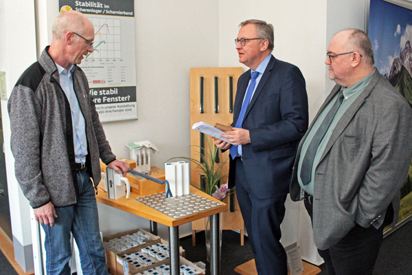 drei Männer, die sich an einem Tisch mit Teilen von Fenstern unterhalten
