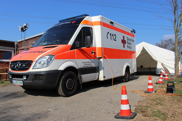 ein Rettungswagen auf einem Kiesweg vor einem Zelt