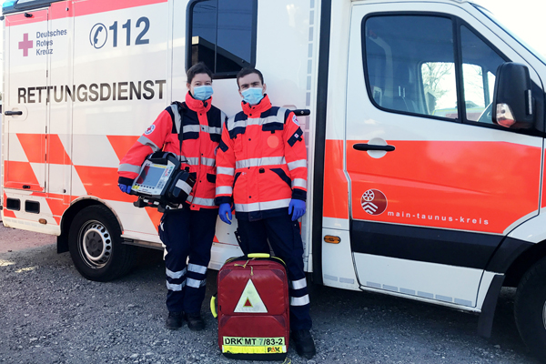 zwei Sanitäter mit Mundschutz vor einem Rettungswagen