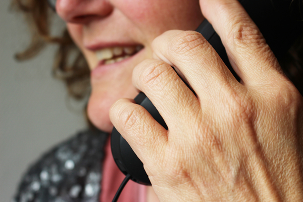 eine Frau, deren untere Gesichtshälfte sichtbar ist und die sich einen Telefonhörer ans Ohr hält